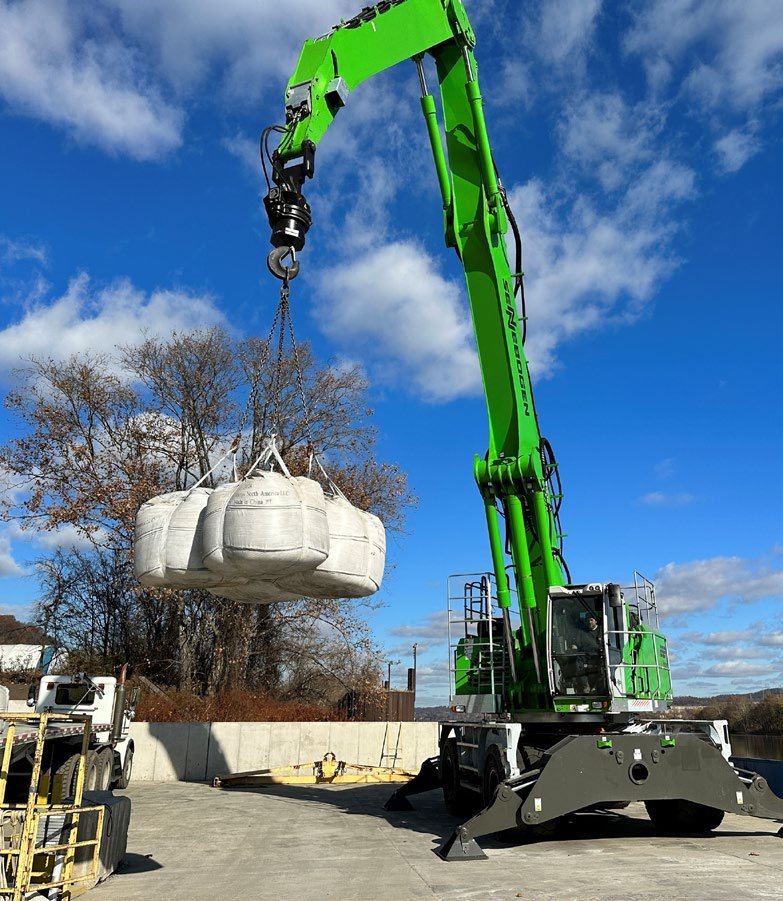 Material handler lifting a bundle of white super sacks against a blue sky